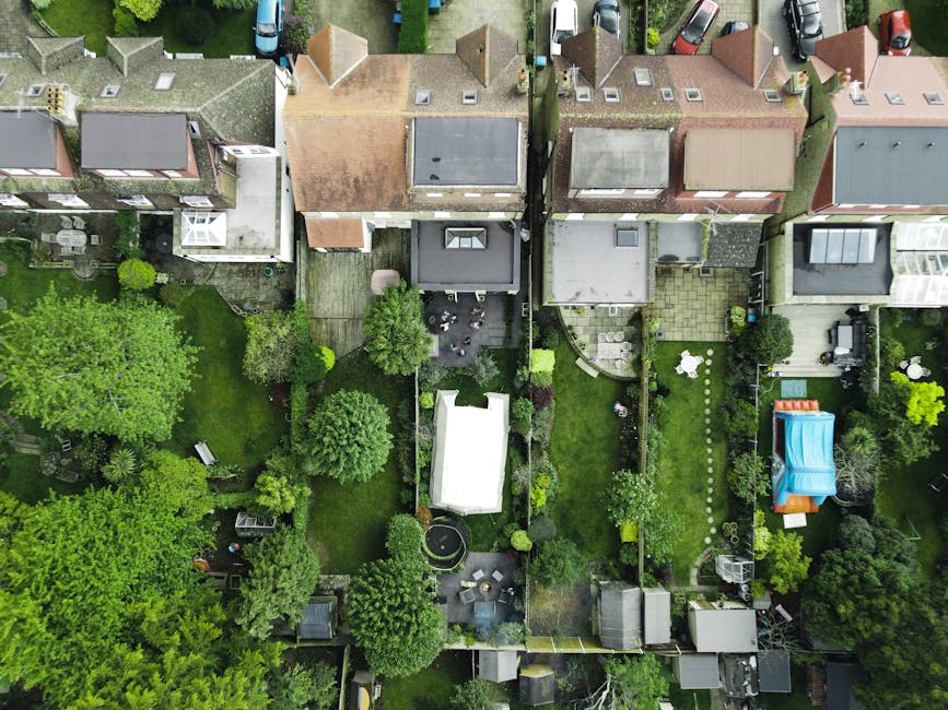 A well-maintained garden scene featuring a lush, neatly trimmed green lawn in the foreground, bordered by diverse flowering and foliage plants. To the left, there are large, broad-leaved hostas with g